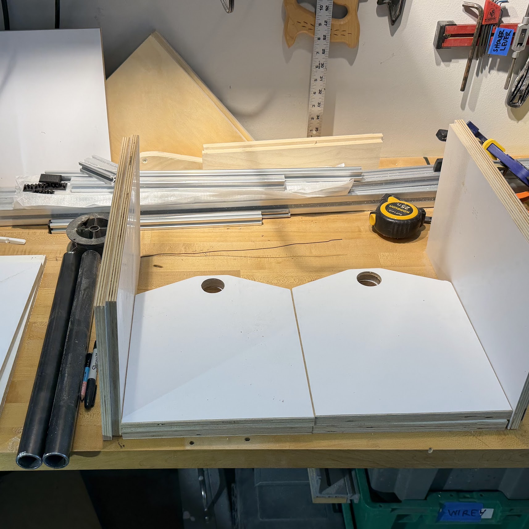 Plywood end caps, sides, and two cut lengths of black steel pipe laid out on a workbench.